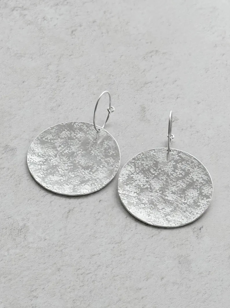 Large sterling silver textured disc hoop earrings.