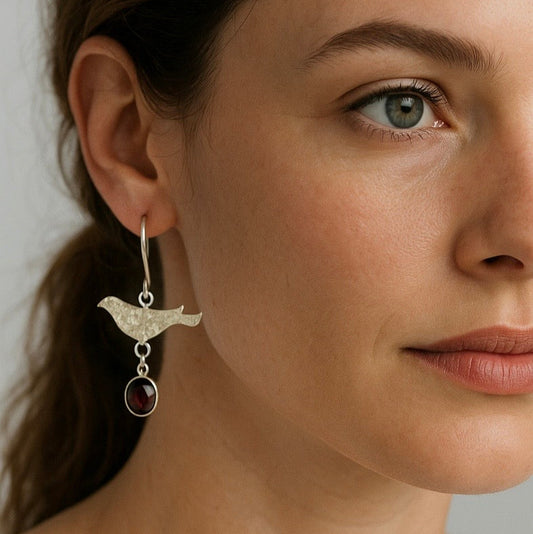 Close-up of a woman wearing a bird-shaped earring with a red stone.