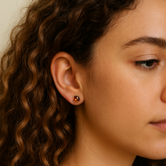 Close-up of a person wearing a sterling silver stud earring with a baltic amber