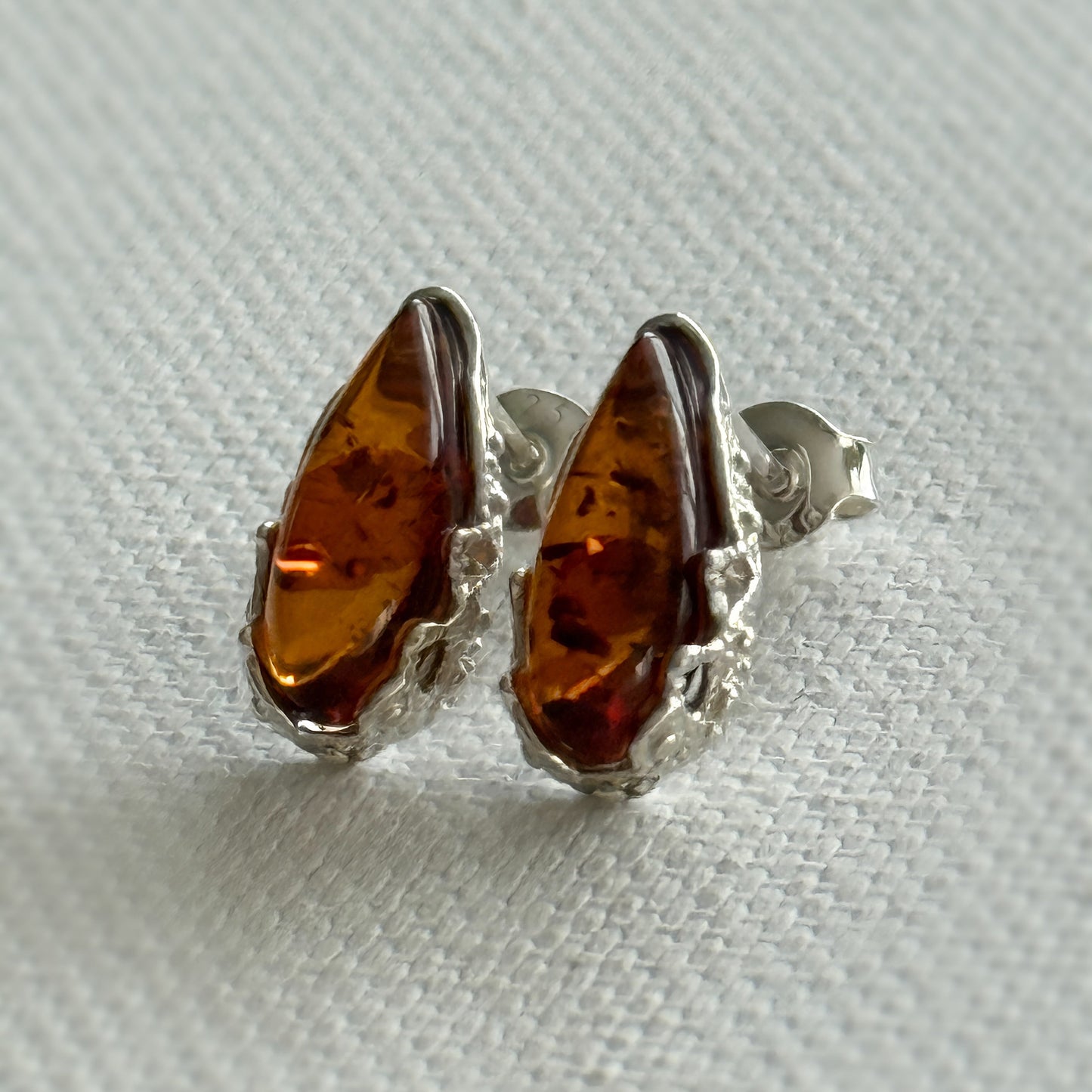 Pair of amber stone earrings with sterling silver settings on a light cream background
