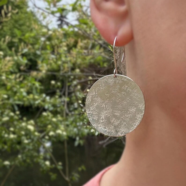 Handmade large sterling silver textured disc earrings, shown worn by a model.