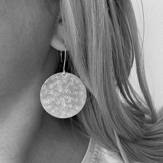 Large handmade sterling silver disc earrings with hammered texture, worn by a model