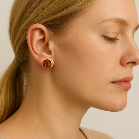 Close-up of a woman wearing a round sterling silver and amber stud earring on a neutral background.