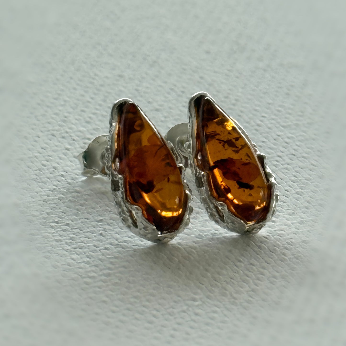 Pair of amber sterling silver teardrop stud earrings on a light cream background