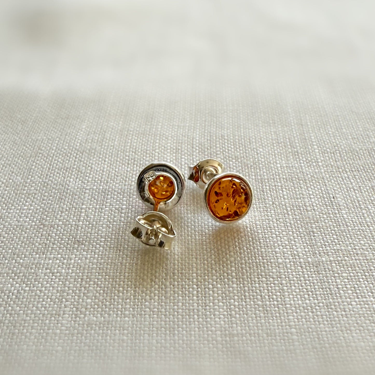 Pair of amber sterling silver stud earrings on a light fabric background