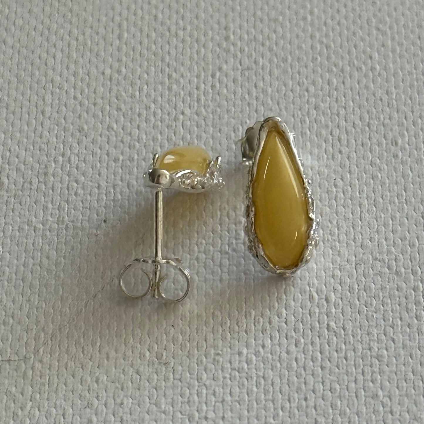 Pair of sterling silver stud earrings with yellow baltic amber teardrop on a white background.