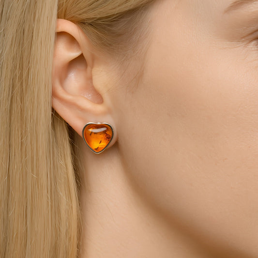 Heart-shaped sterling silver baltic amber earring worn by a person with blonde hair.