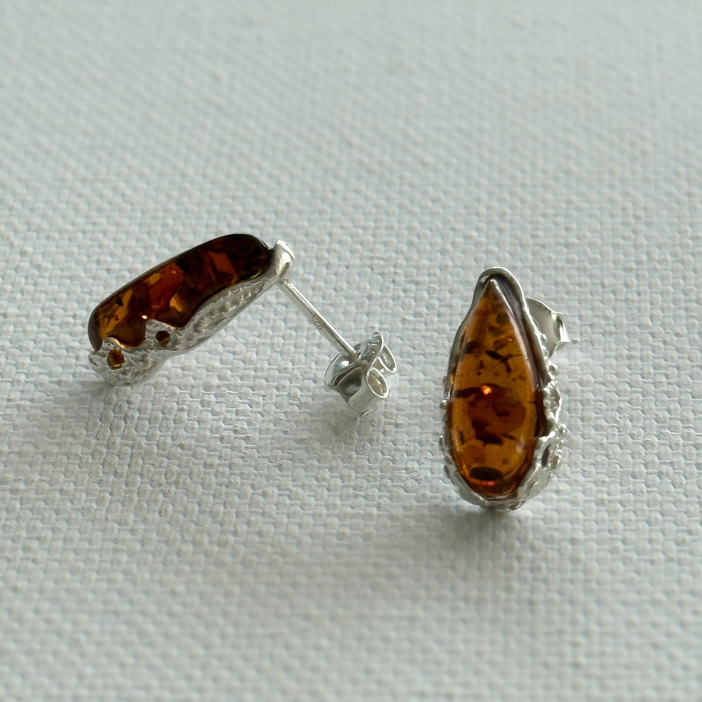 Pair of amber teardrop sterling silver stud earrings on a light cream background.