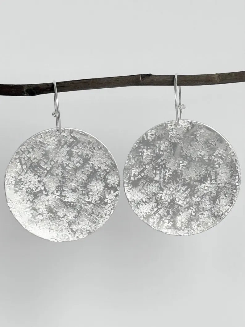 Large sterling silver textured disc hoop earrings featuring hand-hammered discs that catch the light beautifully. Elegant and lightweight, these hypoallergenic earrings are perfect for all-day wear. The silver hoops allow the discs to dangle gracefully, making them a versatile choice for both casual and formal outfits. Thoughtfully packaged in a branded jewellery box, they make an ideal gift for birthdays, anniversaries, or special occasions. Dimensions: 4.7cm long, 3.5cm disc diameter.
