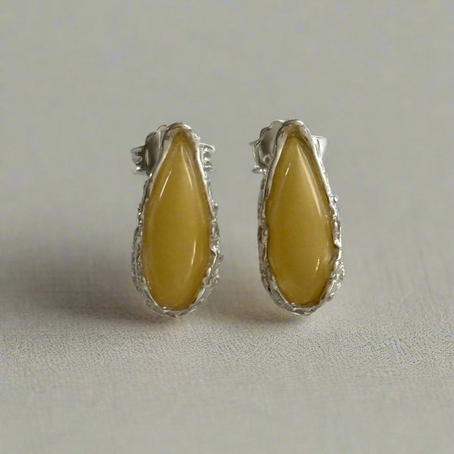 Pair of sterling silver stud earrings with yellow baltic amber on a light white background.
