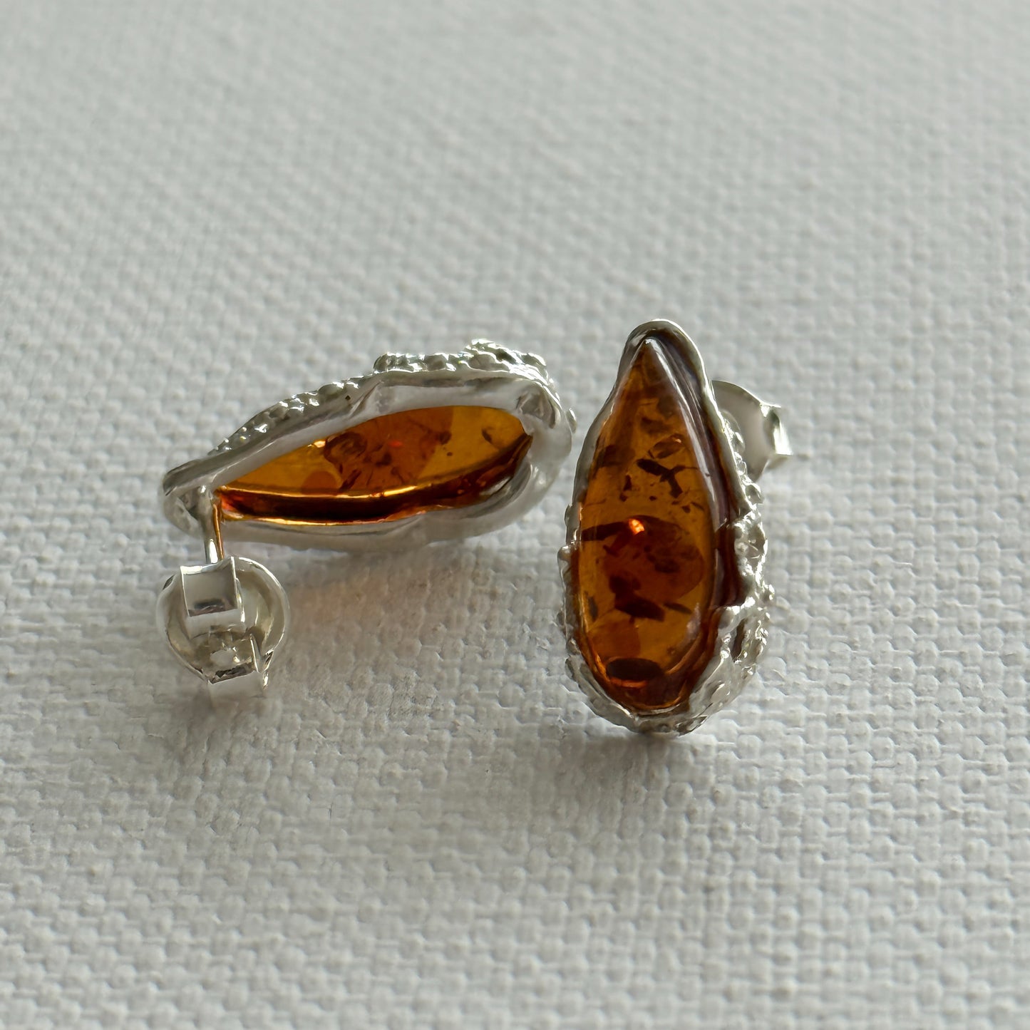 Pair of amber teardrop stud earrings with sterling silver settings on a light cream background