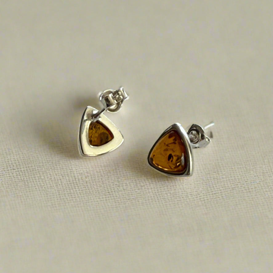pair of sterling silver triangle stud earrings with amber stones on a light background .
