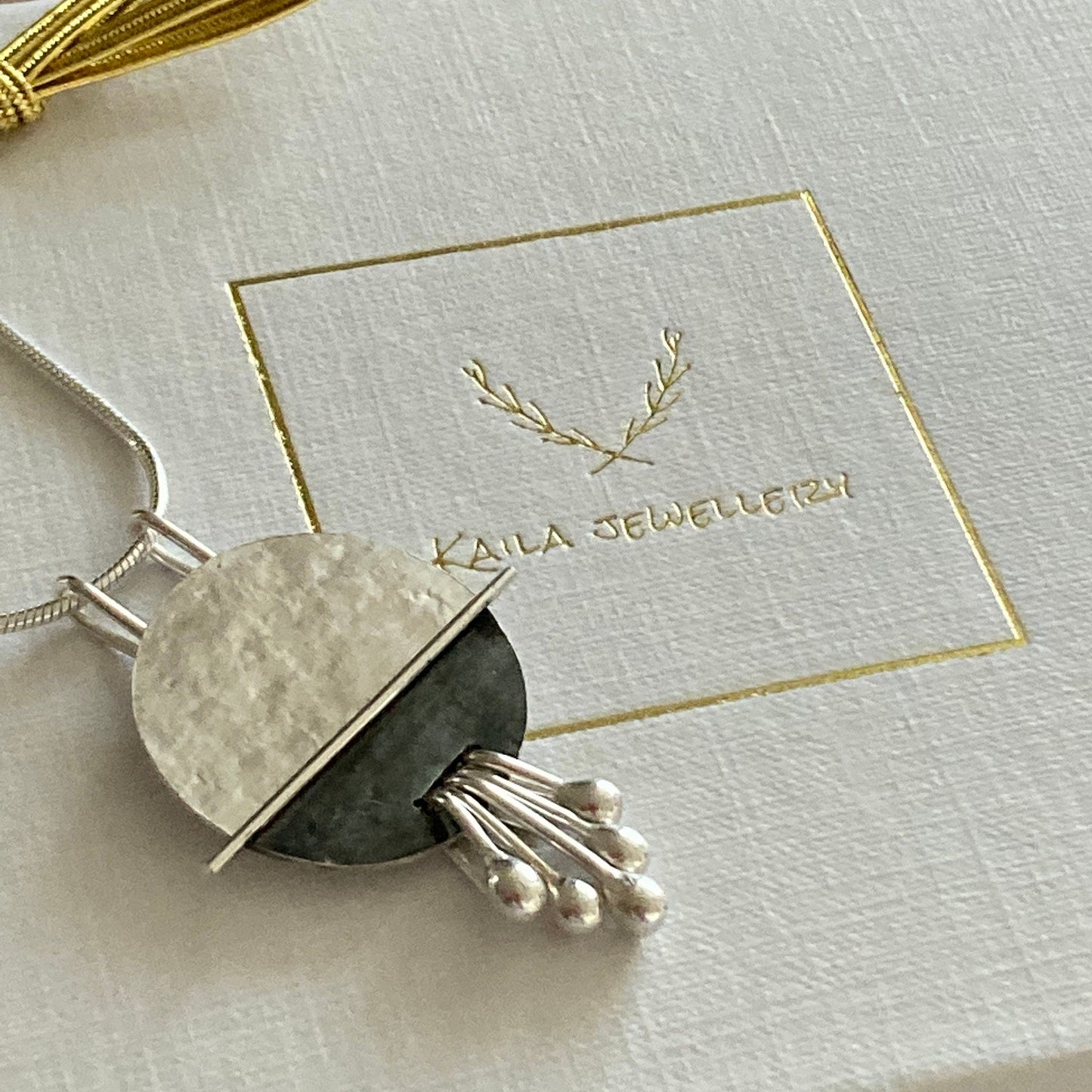 Handmade sterling silver disc pendant necklace with a textured, partially oxidised and polished finish, hanging from a sleek silver snake chain, displayed in a Kaila Jewellery gift box.