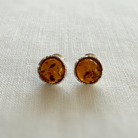 Pair of amber and sterling silver stud earrings on a light fabric background