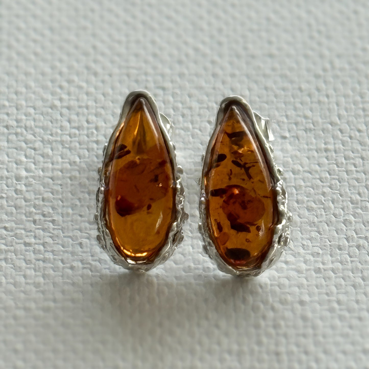 Pair of baltic amber teardrop  stud earrings with sterling silver settings on a light cream background