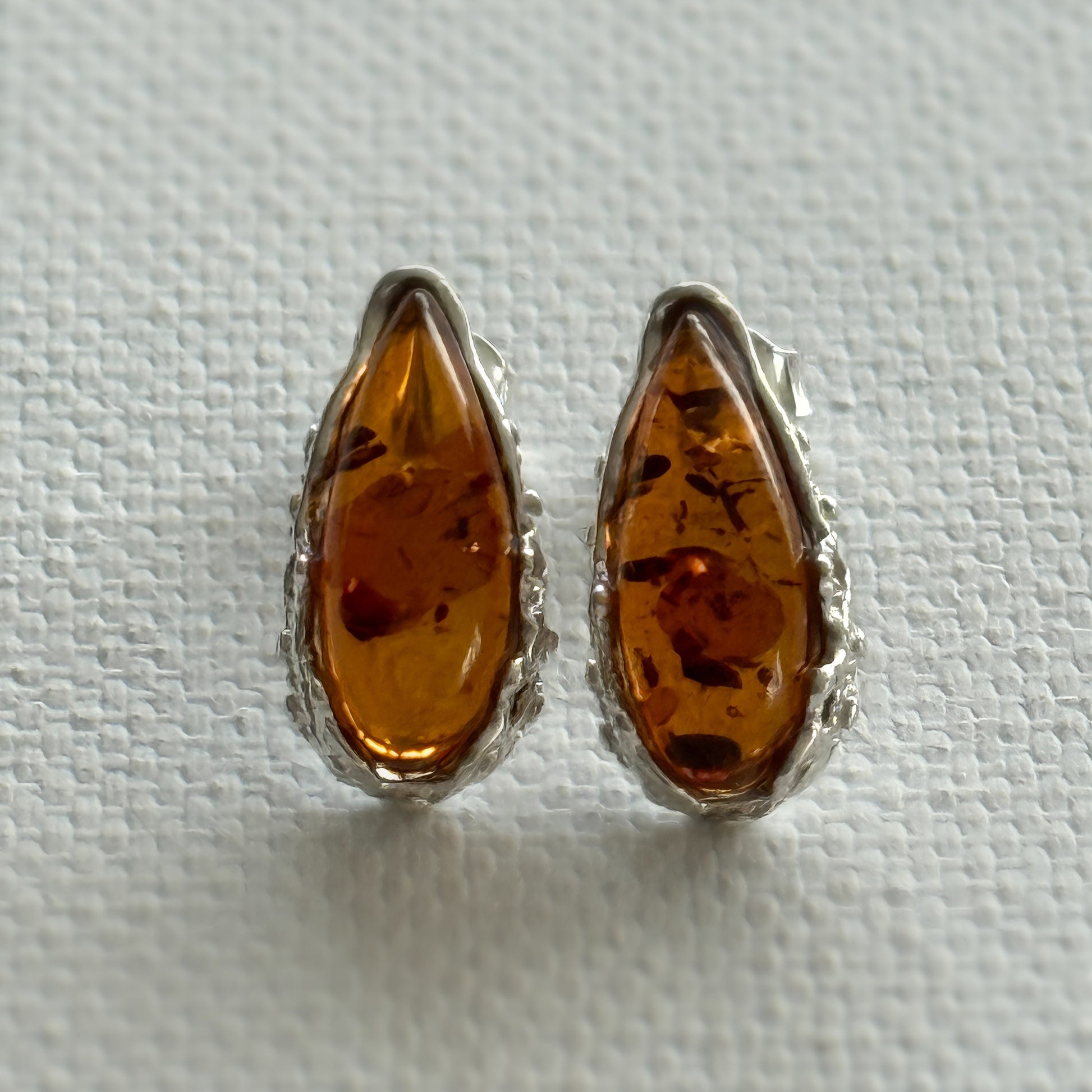 Pair of baltic amber teardrop  stud earrings with sterling silver settings on a light cream background