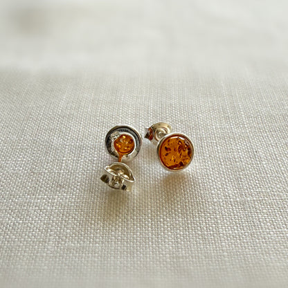 Pair of amber sterling silver stud earrings on a light fabric background