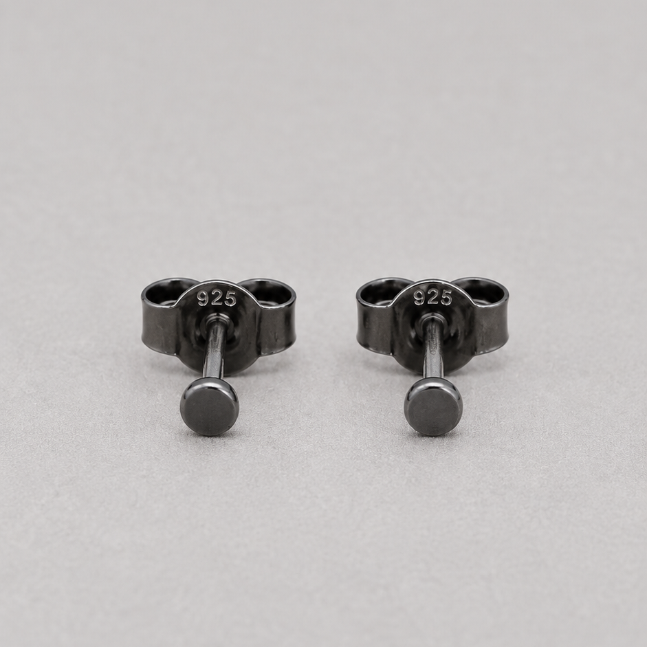 A pair of small black metal stud earrings with a circular front and a screw-back clasp, shown on a light gray background. The earring hardware is stamped with '925', indicating sterling silver.