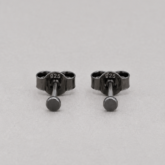 A pair of small black metal stud earrings with a circular front and a screw-back clasp, shown on a light gray background. The earring hardware is stamped with '925', indicating sterling silver.