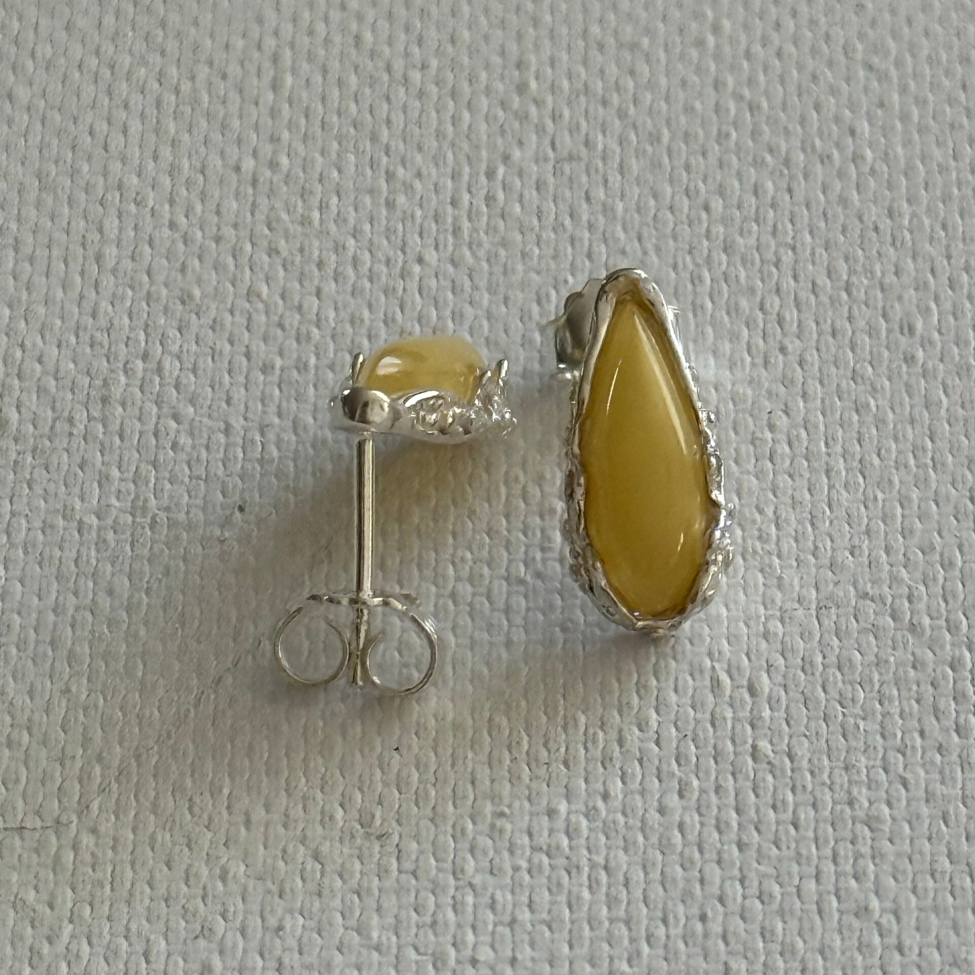 Pair of sterling silver stud earrings with yellow baltic amber teardrop on a white background.