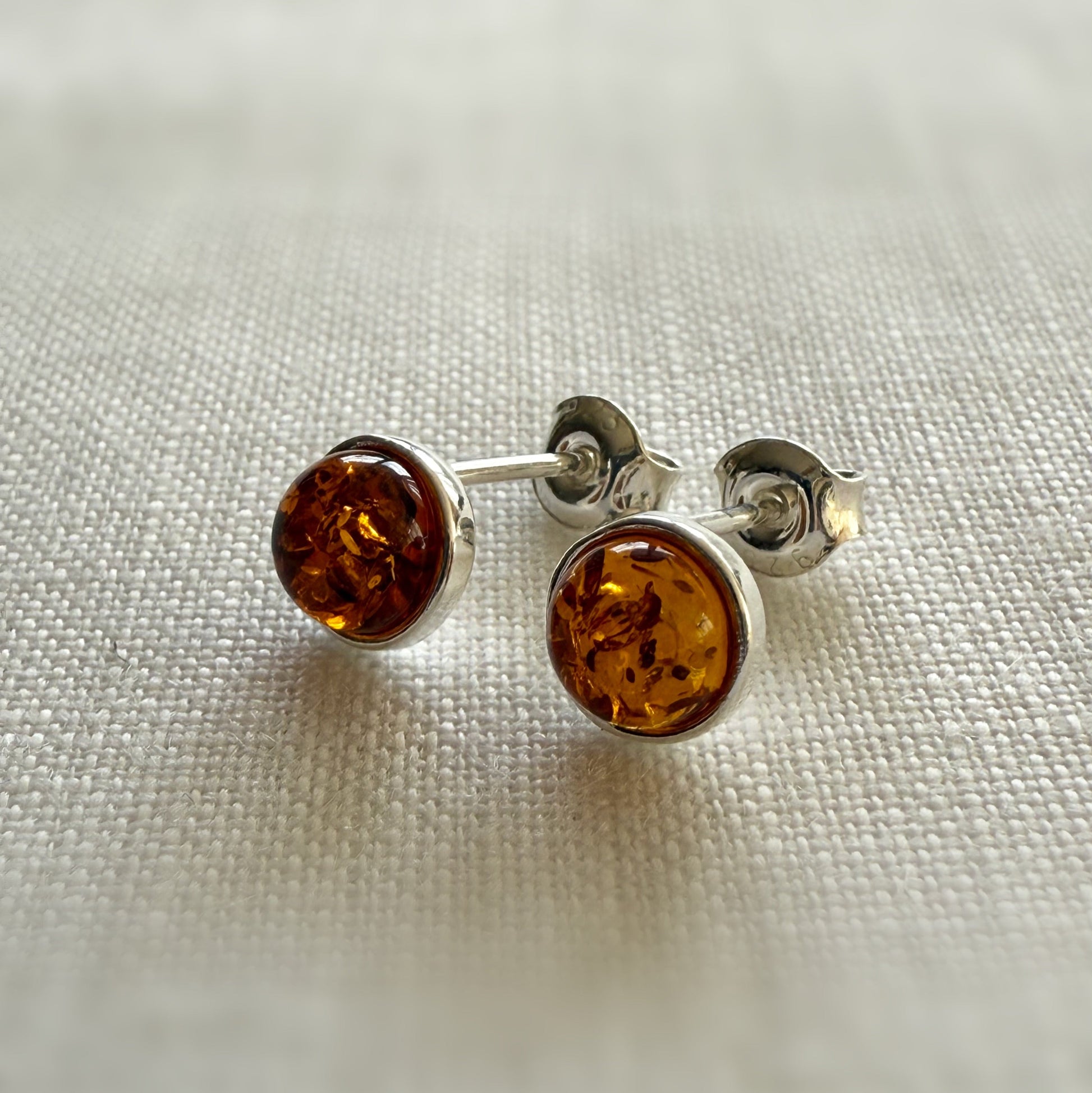 Pair of amber sterling silver stud earrings on a light fabric background.