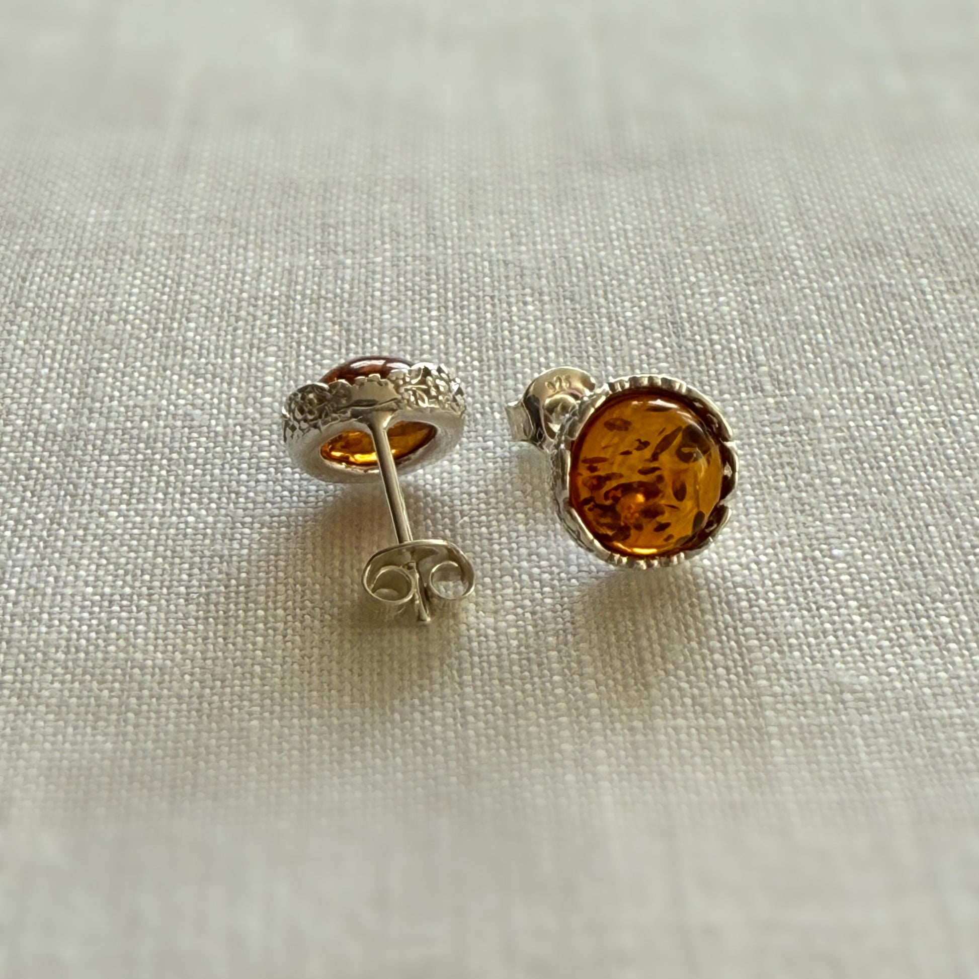 Pair of amber and sterling silver stud earrings on a light fabric background
