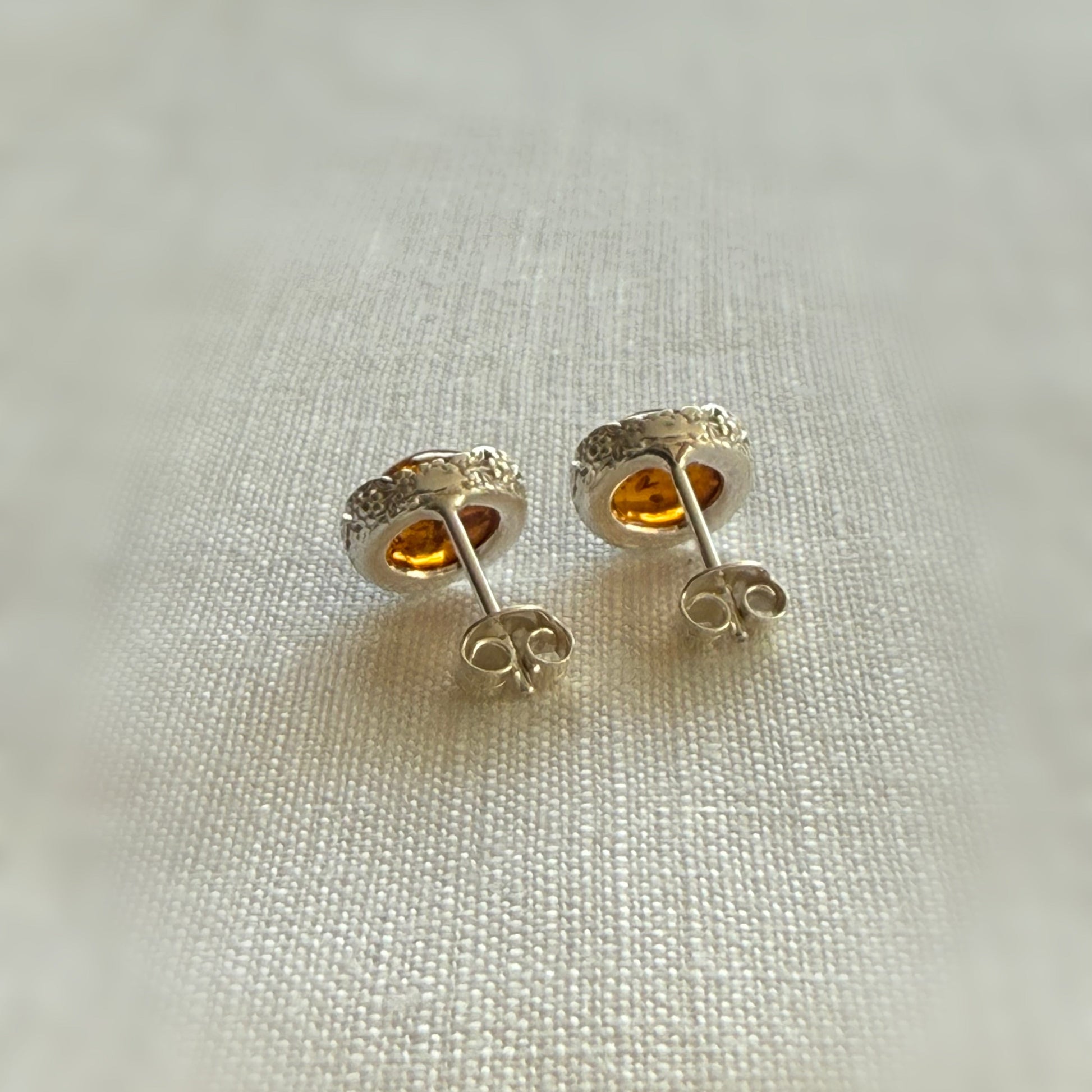 Pair of silver stud earrings with amber on a light fabric background