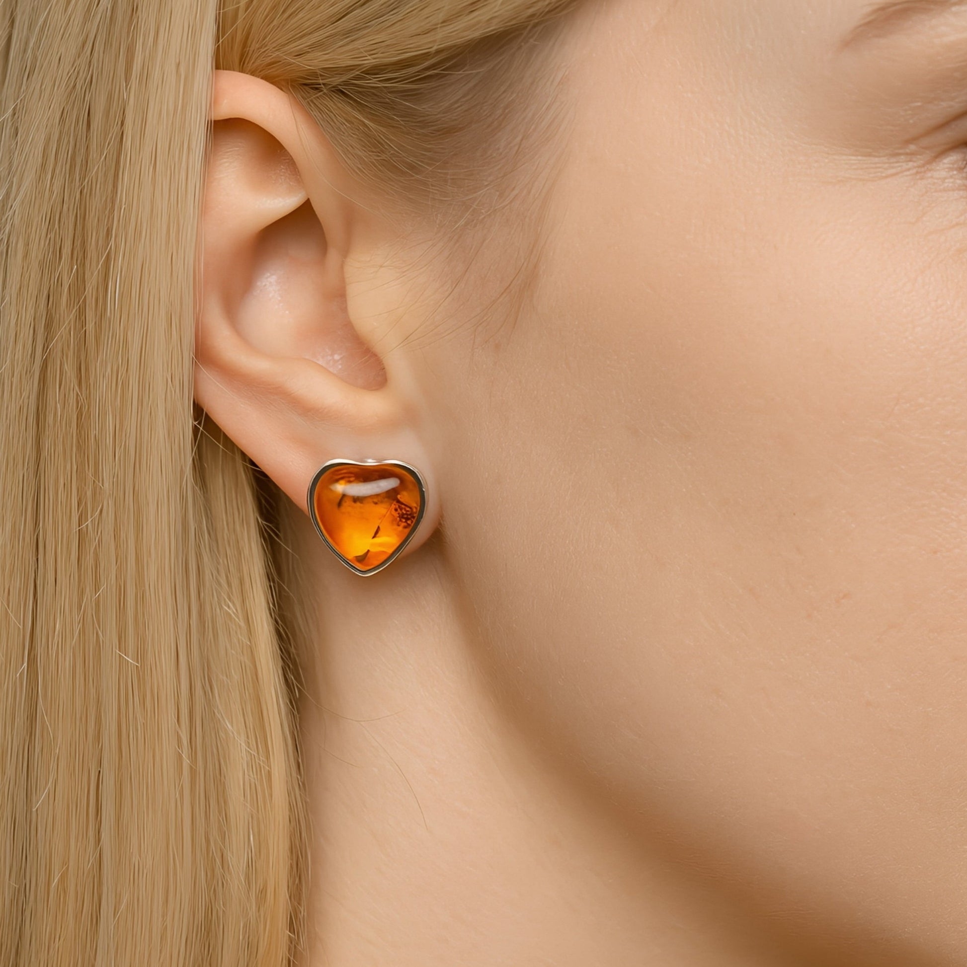 Heart-shaped sterling silver baltic amber earring worn by a person with blonde hair.