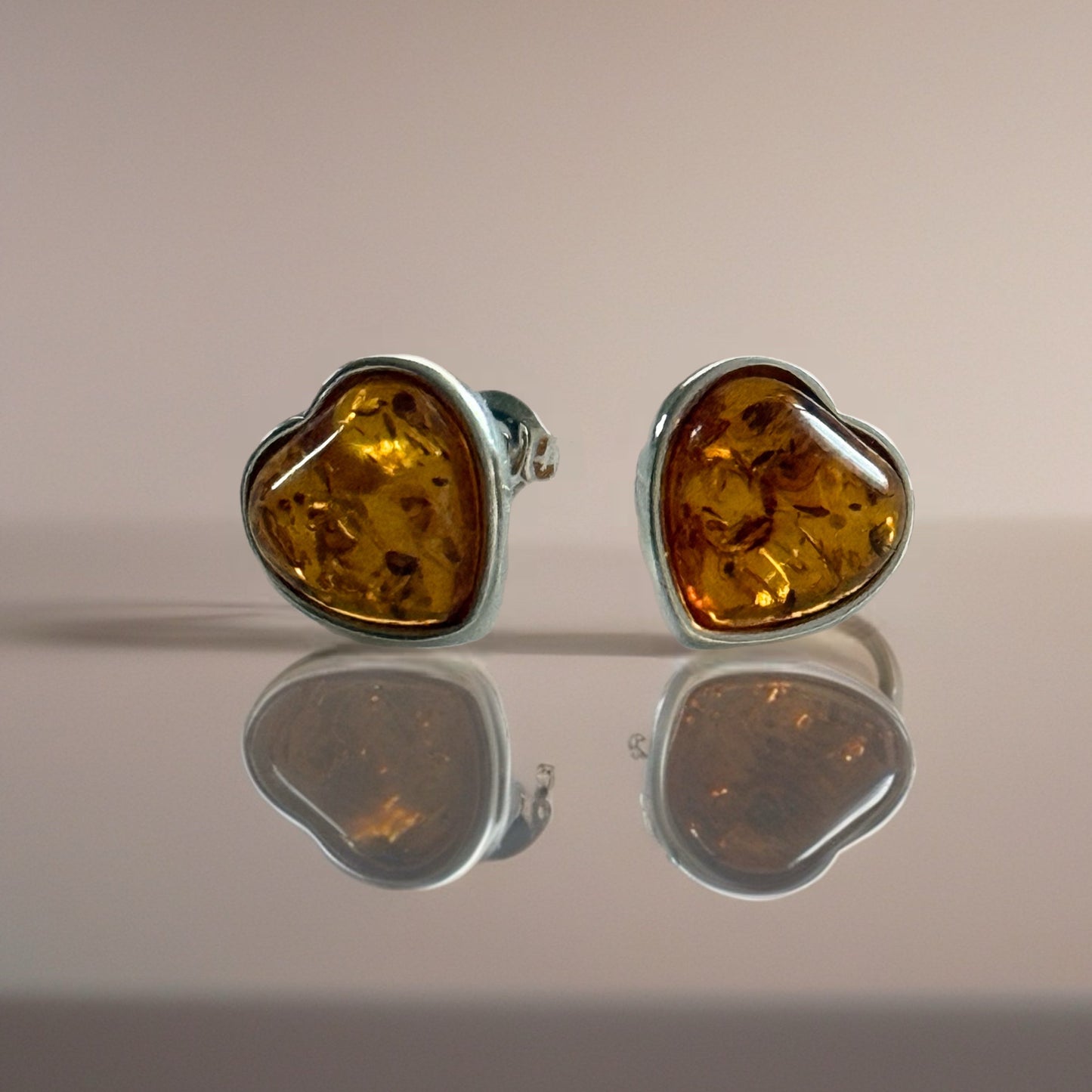 Pair of amber heart-shaped stud earrings on a reflective surface with a neutral background