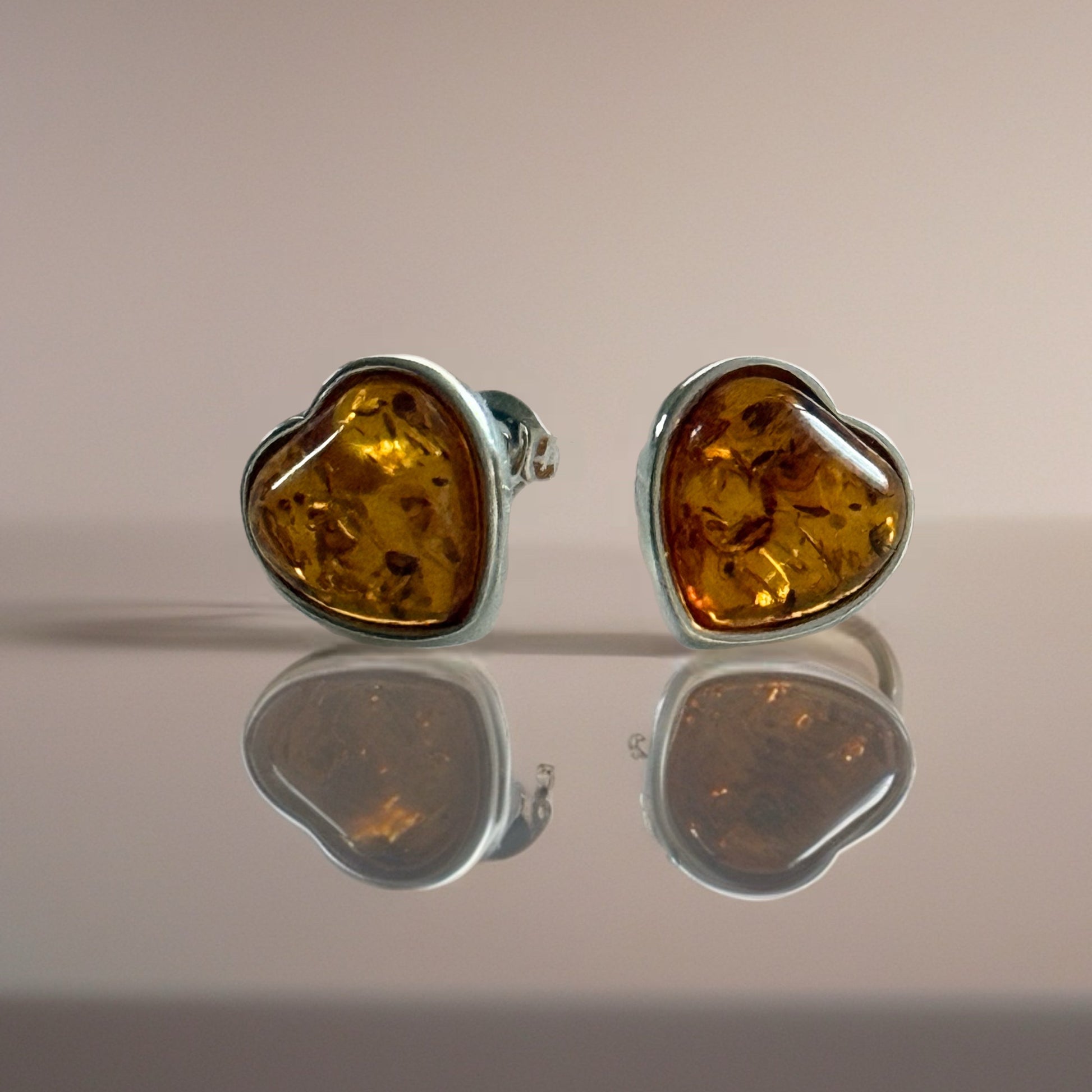 Pair of amber heart-shaped stud earrings on a reflective surface with a neutral background