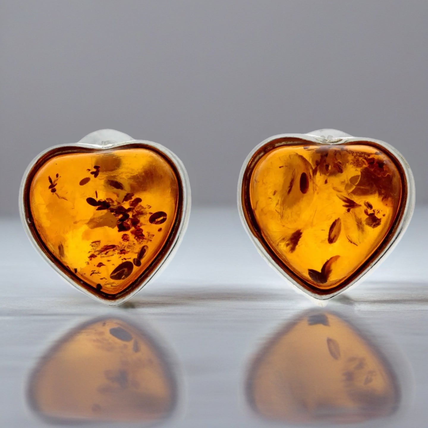 Heart-shaped amber earrings with silver settings on a reflective surface.
