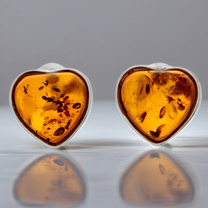 Heart-shaped amber earrings with silver settings on a reflective surface.