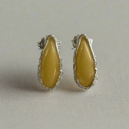 Pair of sterling silver stud earrings with yellow baltic amber on a light white background.