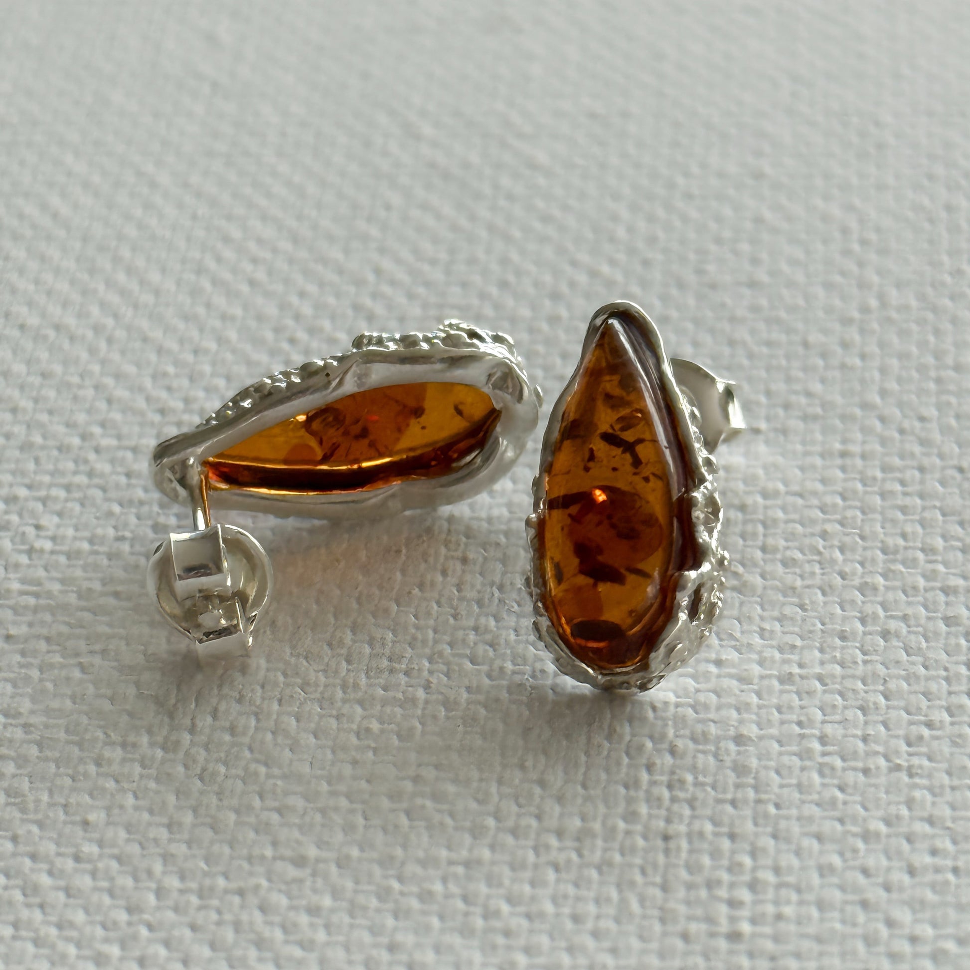 Pair of amber teardrop stud earrings with sterling silver settings on a light cream background